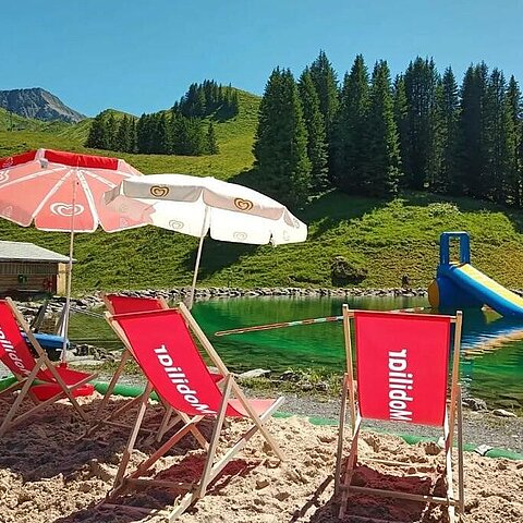 Liegestühle und Sonnenschirme im Sand beim See