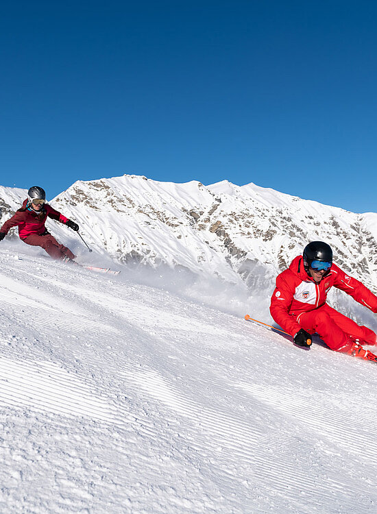 Zwei Skifahrer mit Skilehrer auf Skipiste