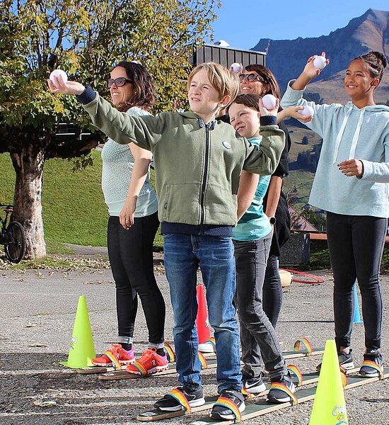 Drei Kinder und zwei Erwachsene welche ein Spiel mit Bällen und Holzski spielen